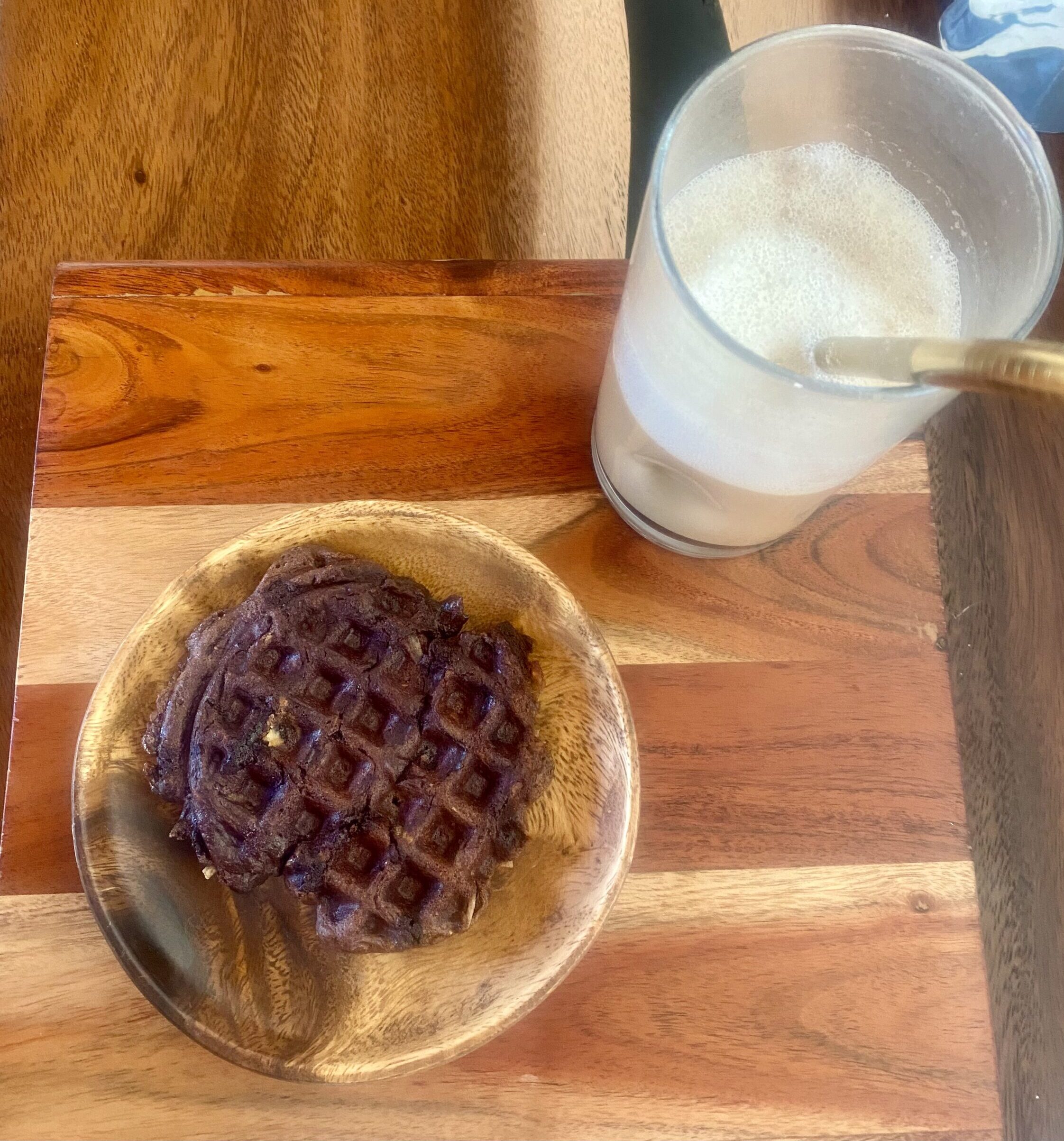 a tiny chocolate waffle on a wooden plate on a wooden desk, with half a glass of coffee