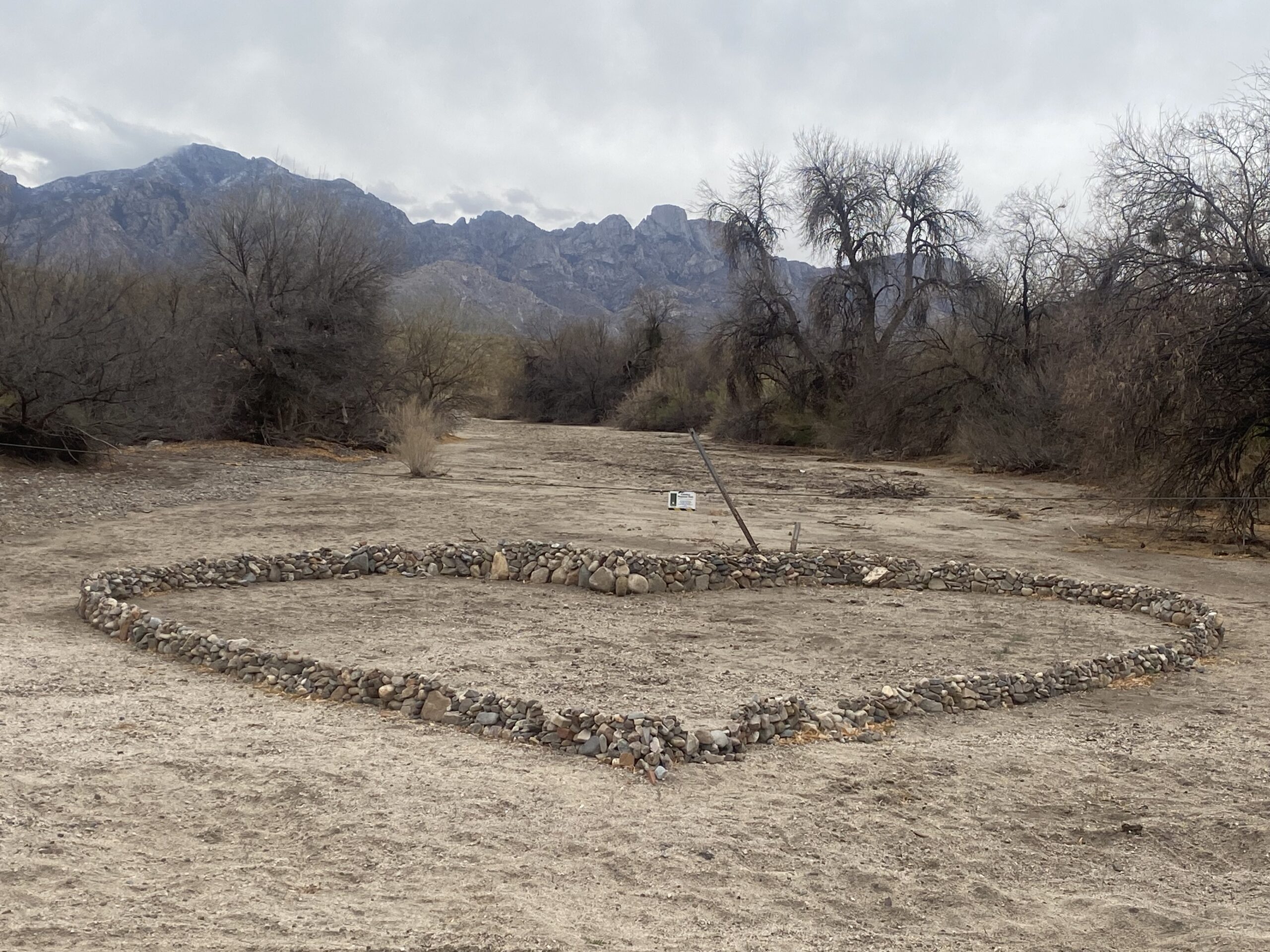 a giant heart-shape made of stones by the side of a dirt road on a stormy desert day