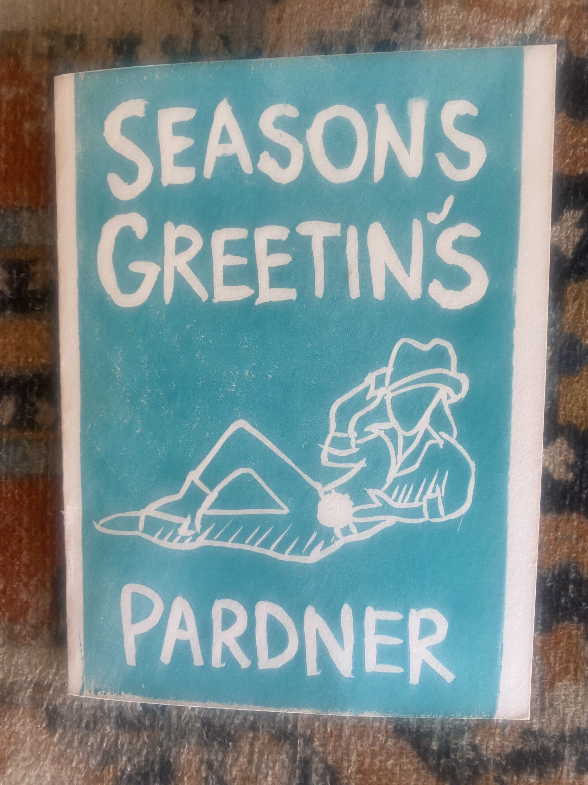 a turquoise card featuring a drawing of a reclining androgynous cowboy says SEASONS GREETINGS, PARDNER”/></p>
<div class=